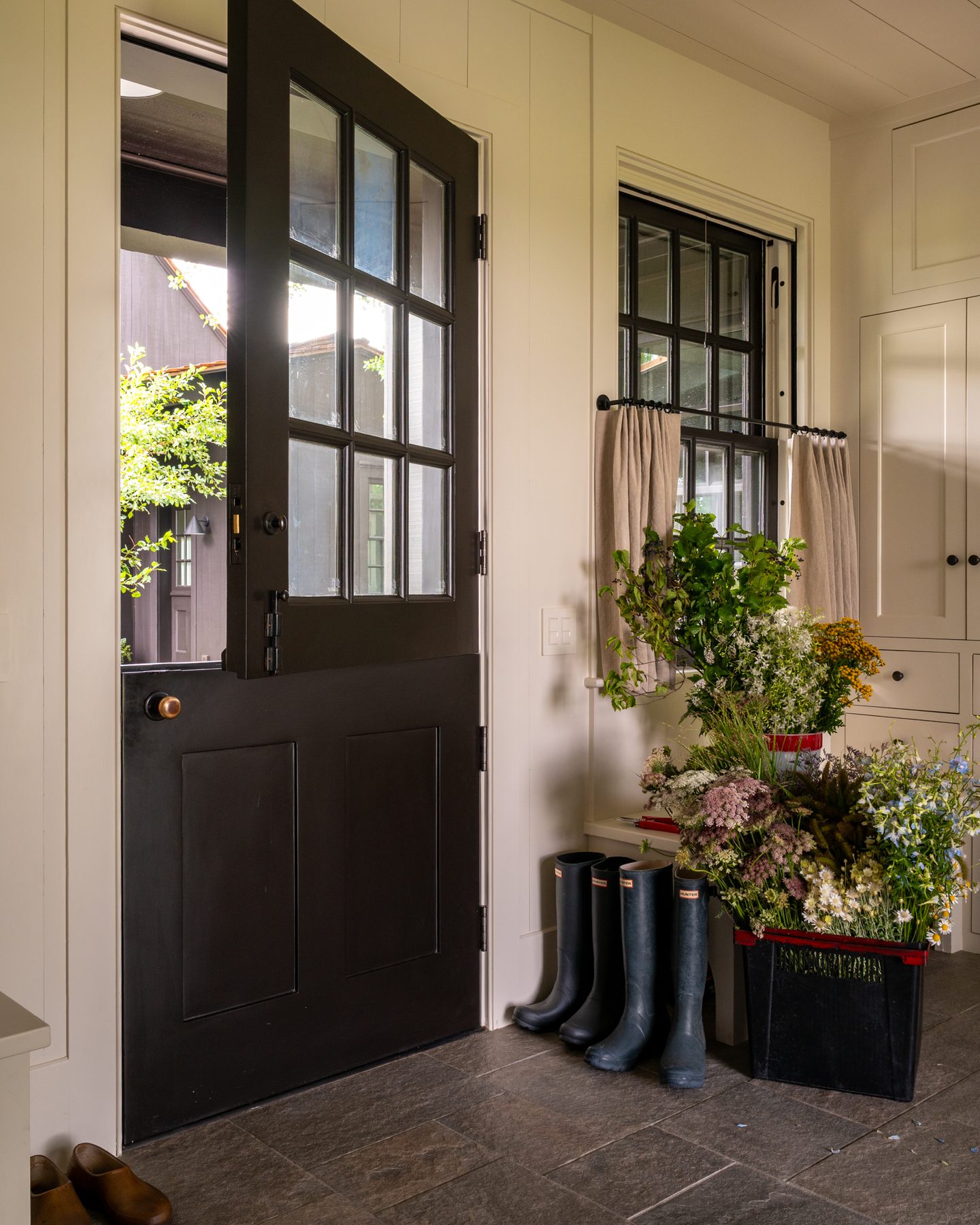Mudroom entry with an open Dutch door, a row of Hunter boots, and bins of just-cut wildflowers along the built-in cabinetry.