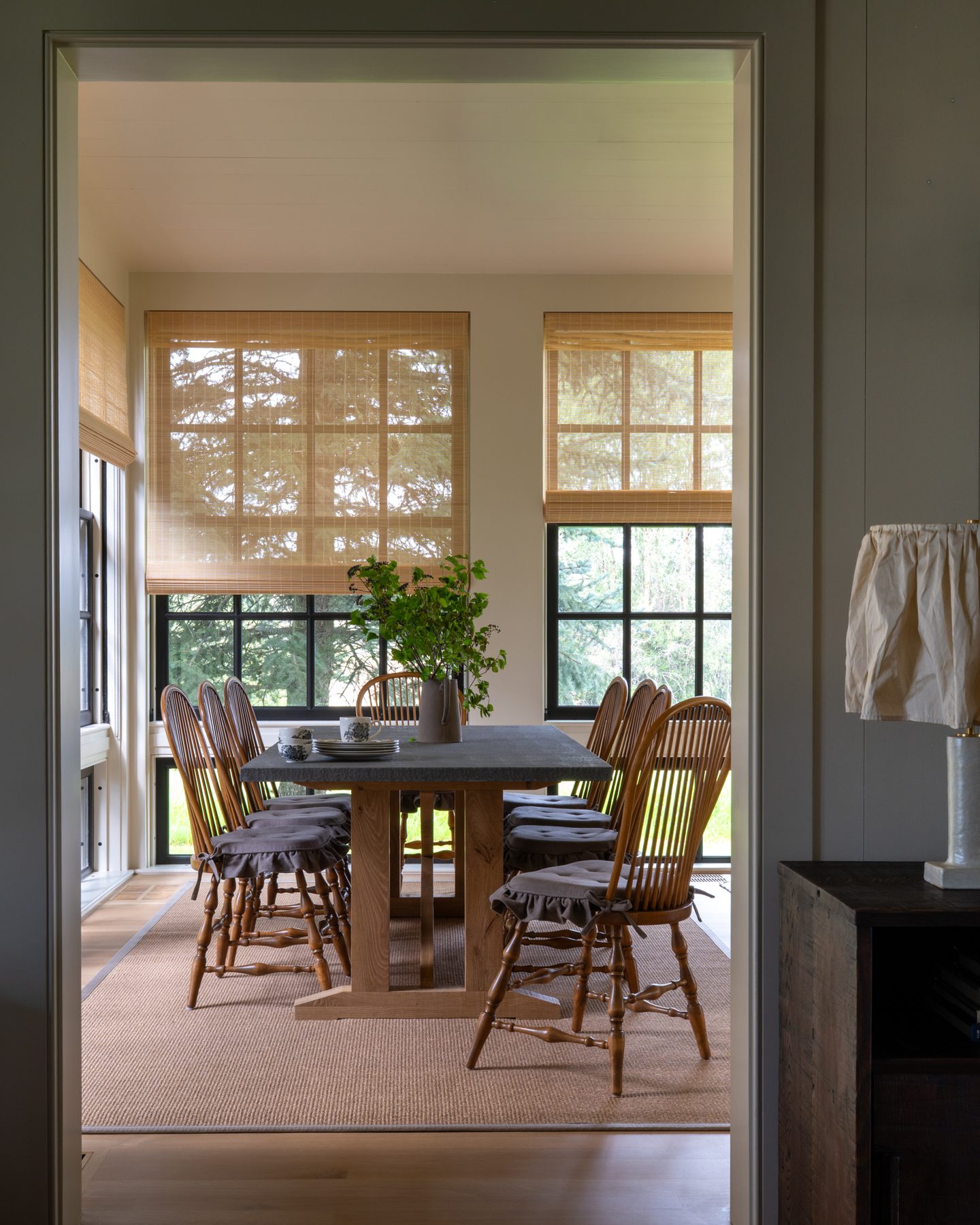 Breakfast nook glimpsed through a doorway, with a stone-topped oak table, Windsor chairs, and a wildflower arrangement.