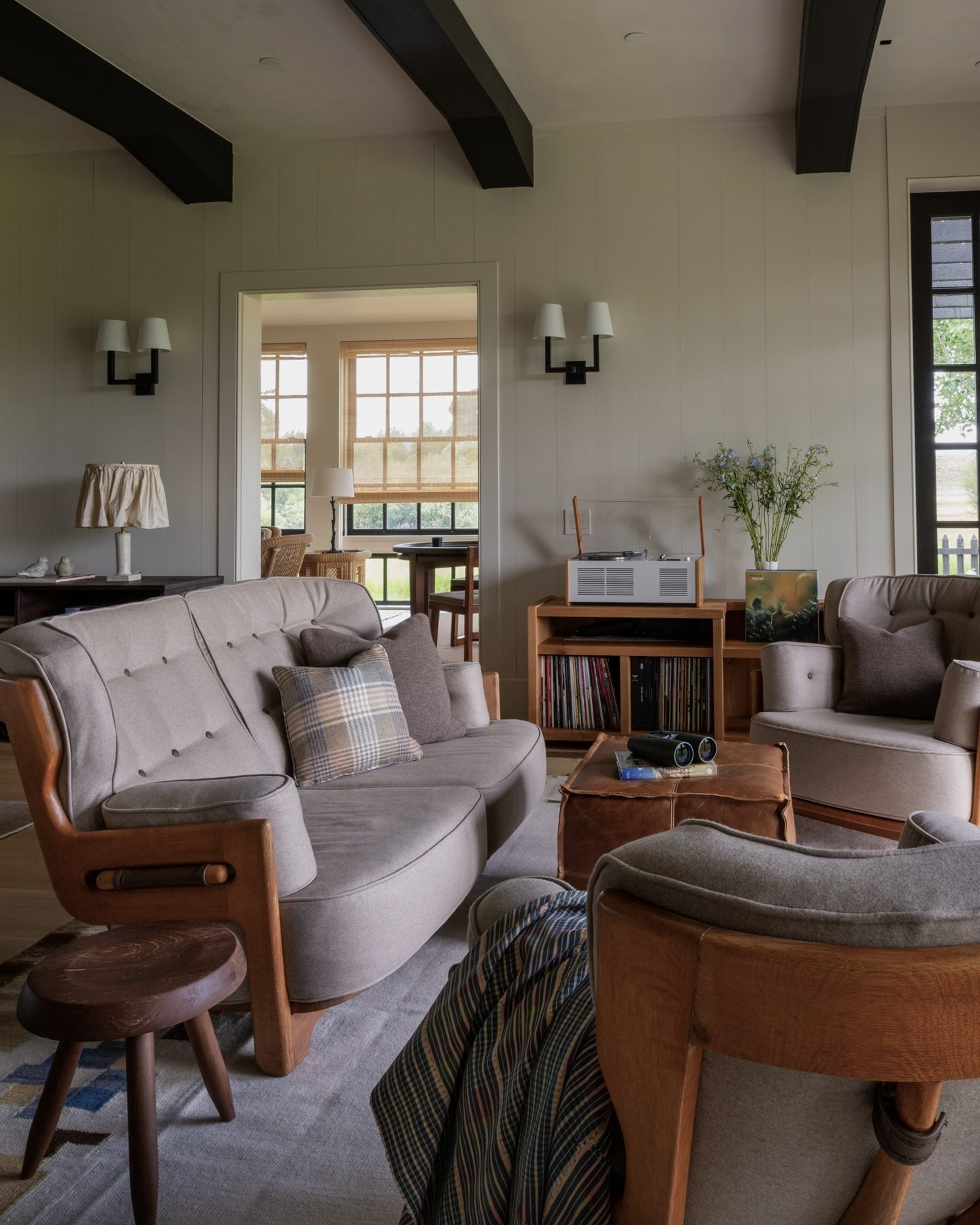 Den with tufted wool sofas, a record player and album collection on a wood console, and a leather-topped ottoman.