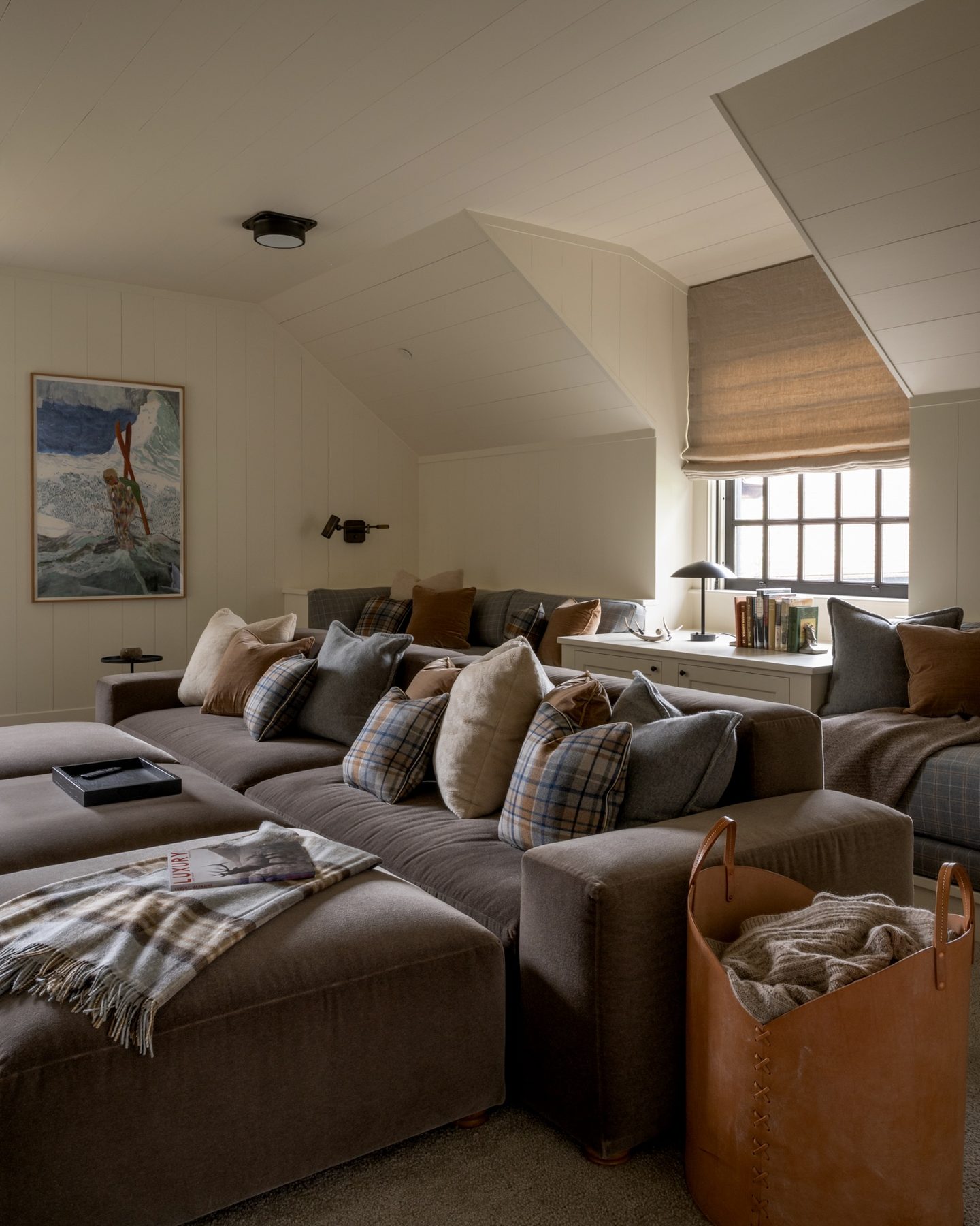 Upstairs bonus room with a deep sectional sofa piled in plaid and mohair pillows, and a vintage ski watercolor on the wall.