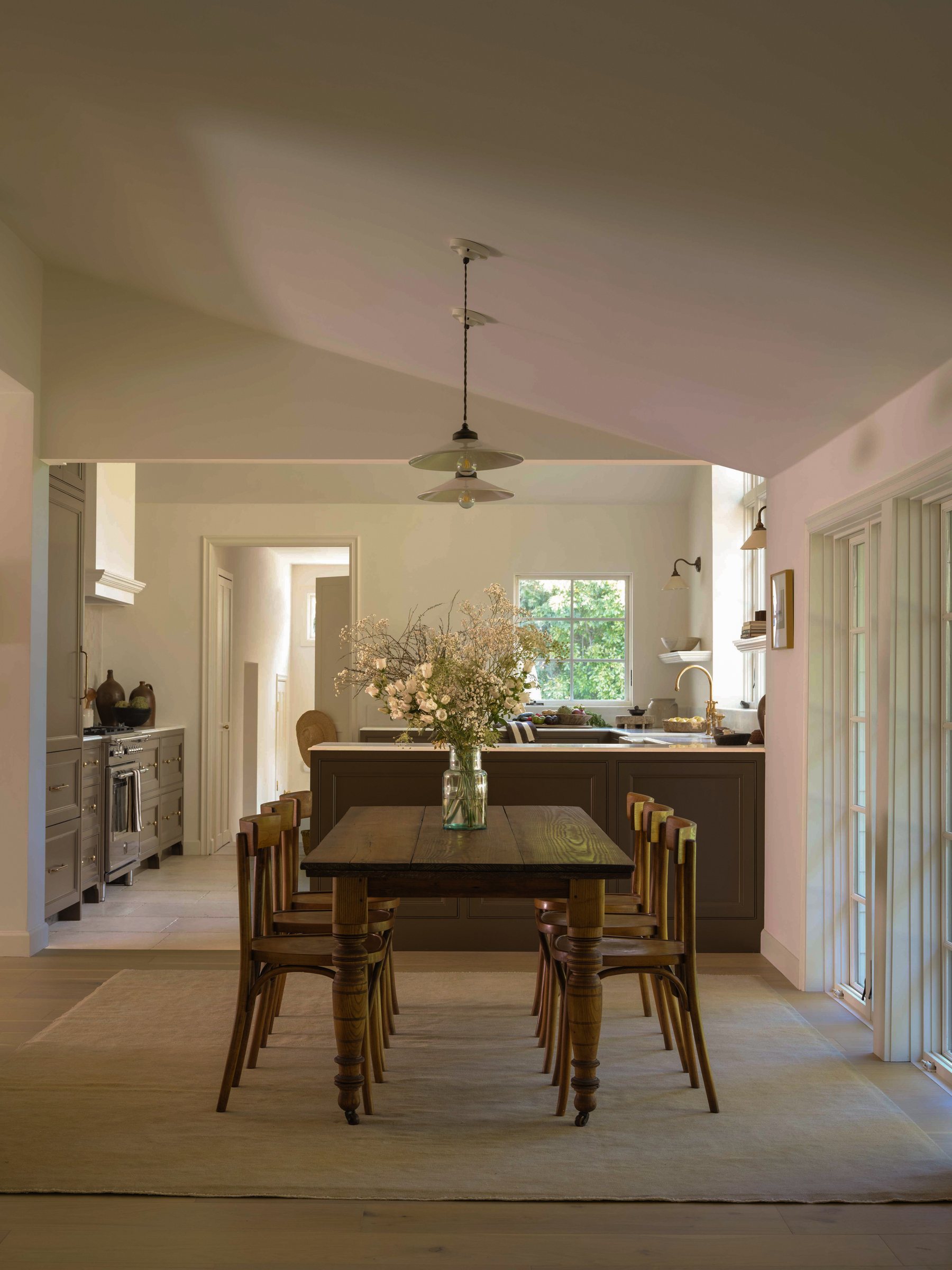 Dining table with bentwood chairs beneath a double pendant light, kitchen visible beyond.