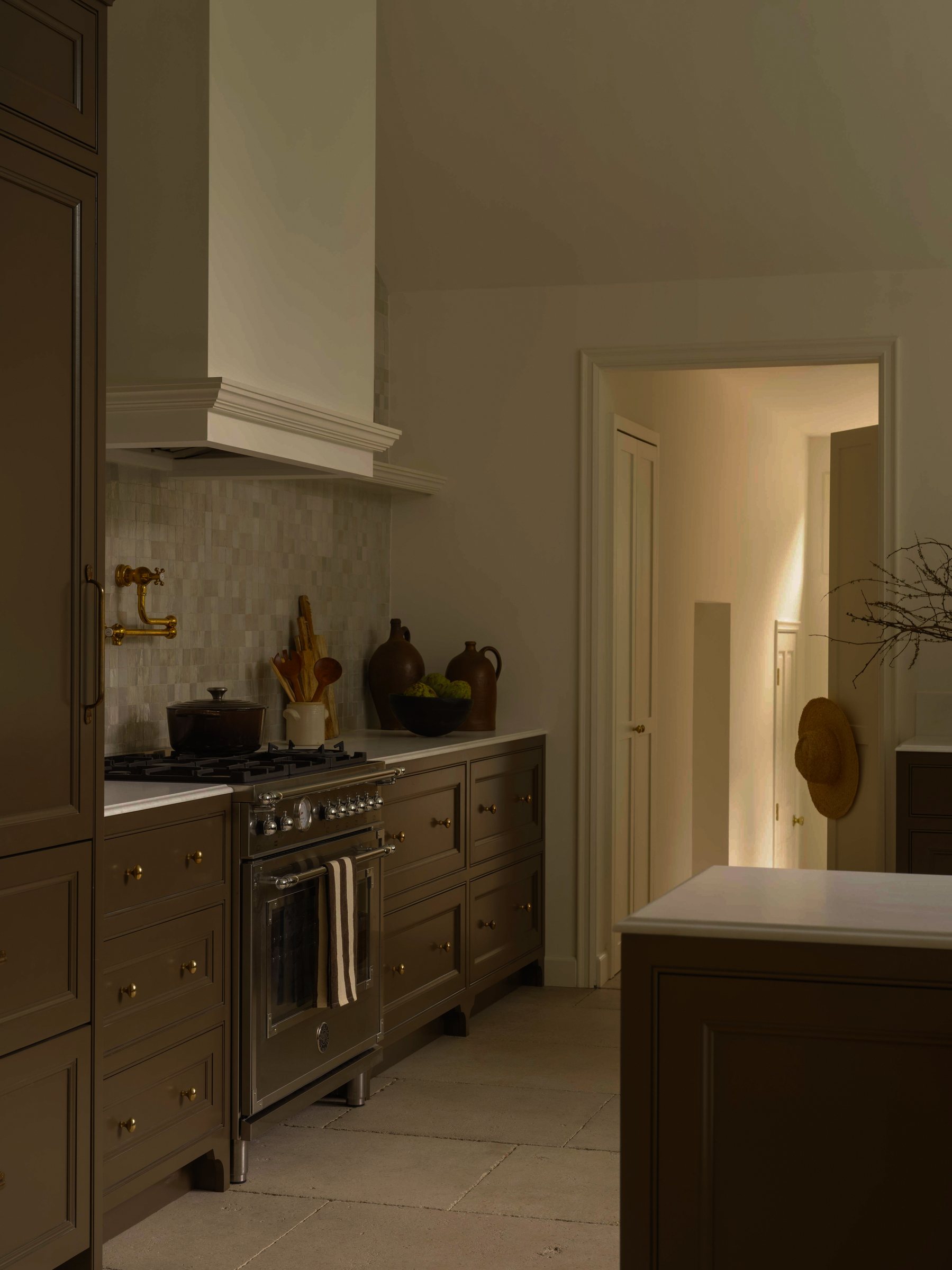 Kitchen with olive cabinetry, brass pot filler, and tile backsplash beside a hallway view.