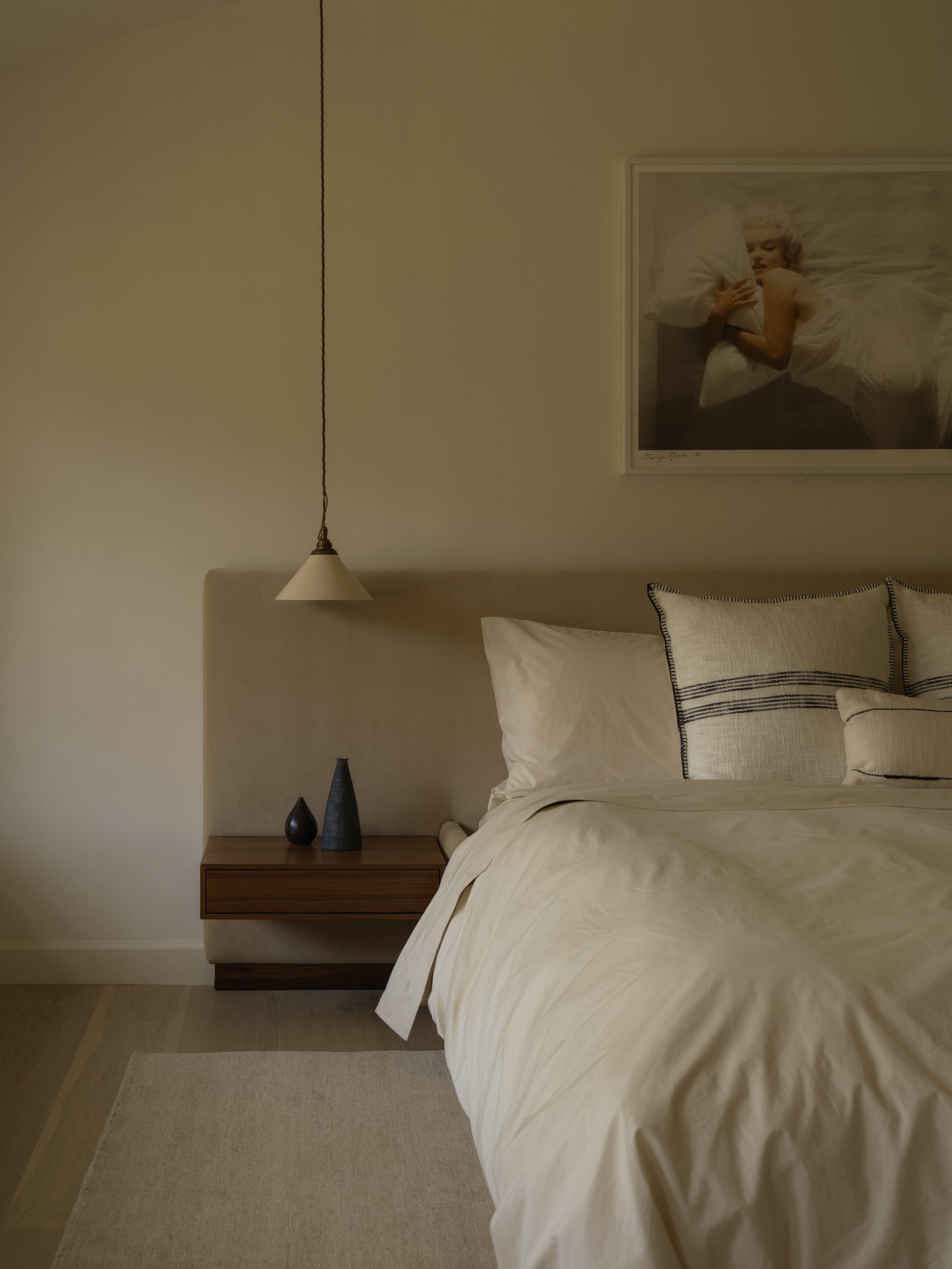 Bed with striped linen pillows beneath a framed photograph, pendant light beside the headboard.