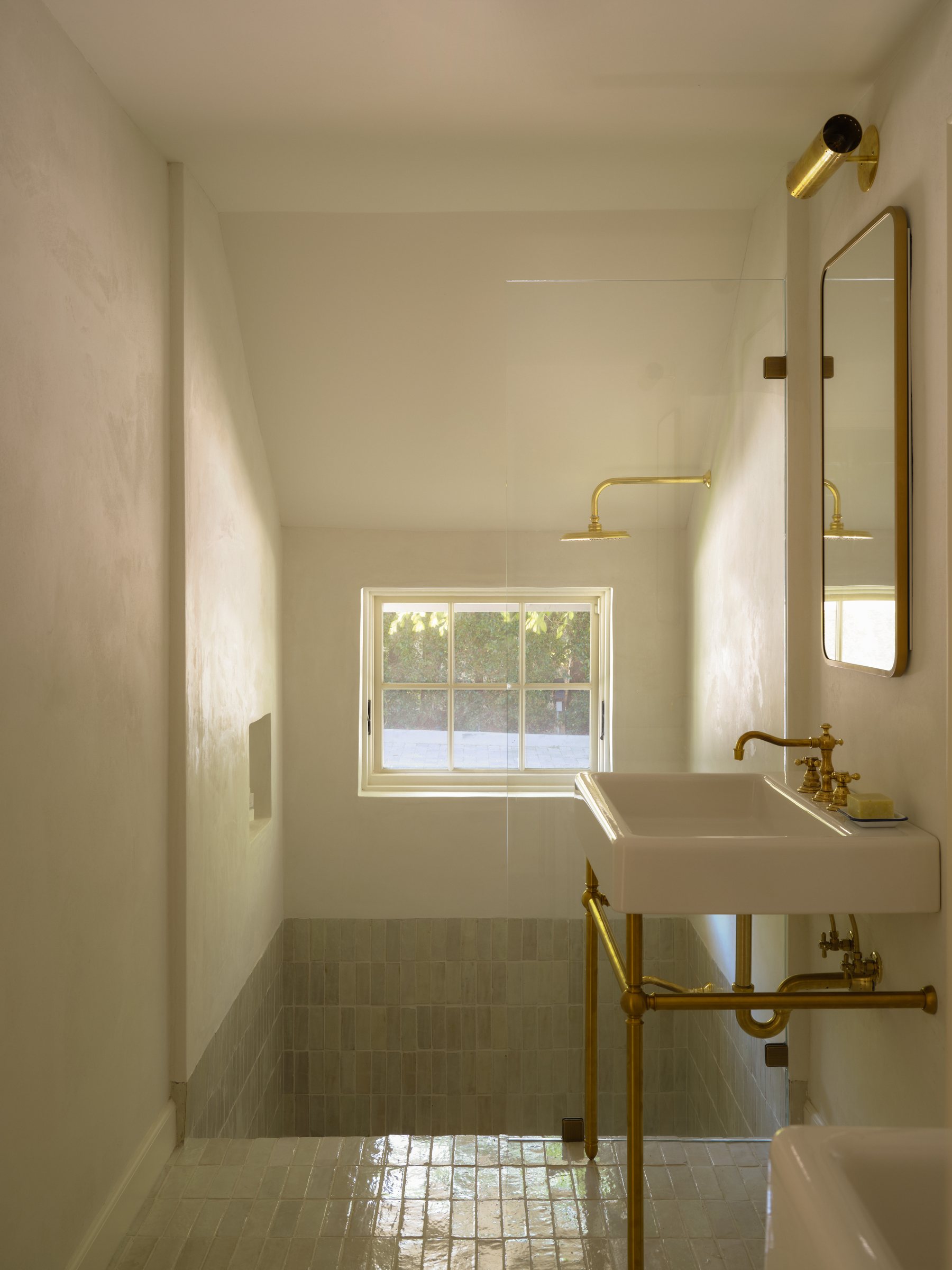 Walk-in shower with brass fixtures, a window, and zellige tile floor.