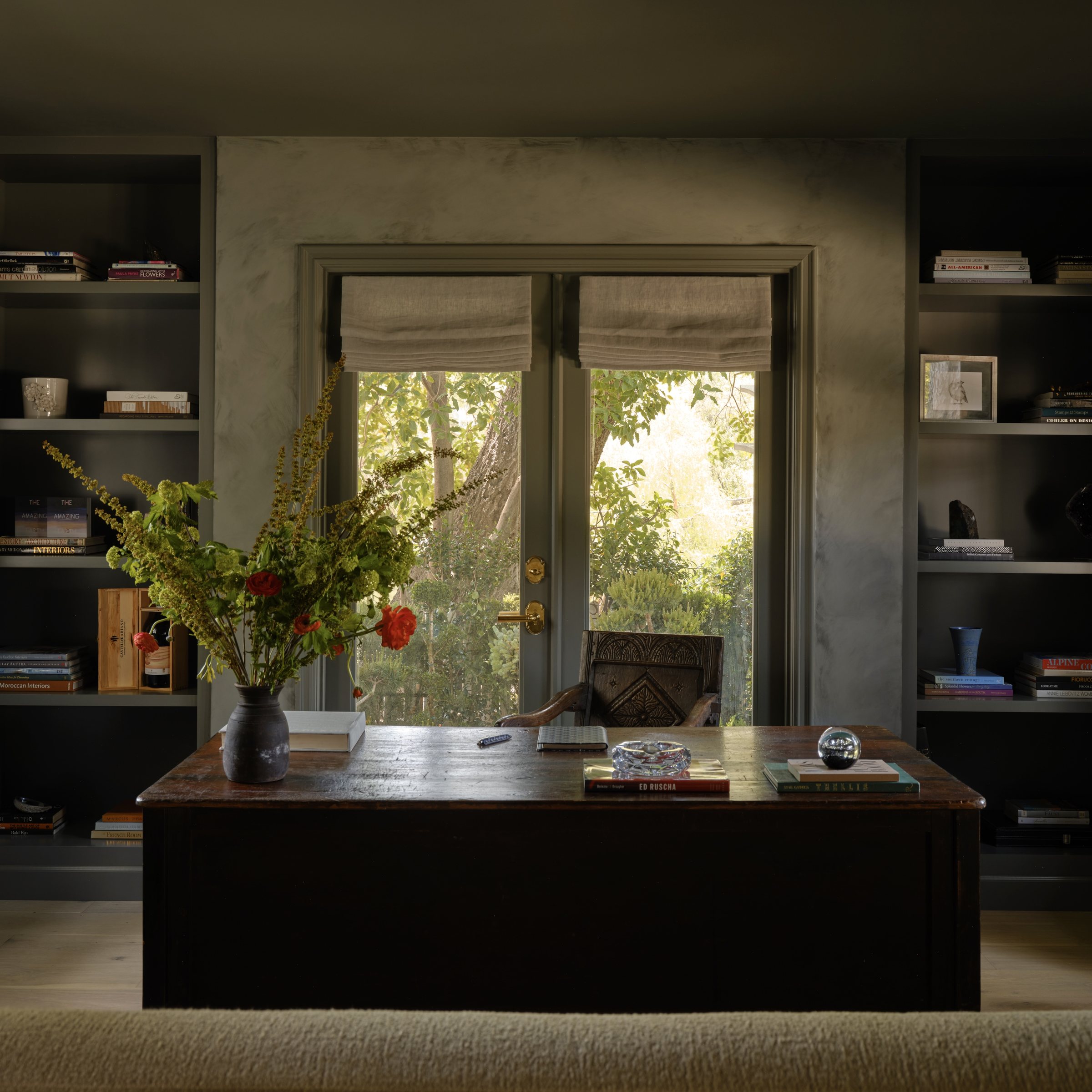 Home office nook with a wood desk, built-in bookshelves, and French doors open to the garden.