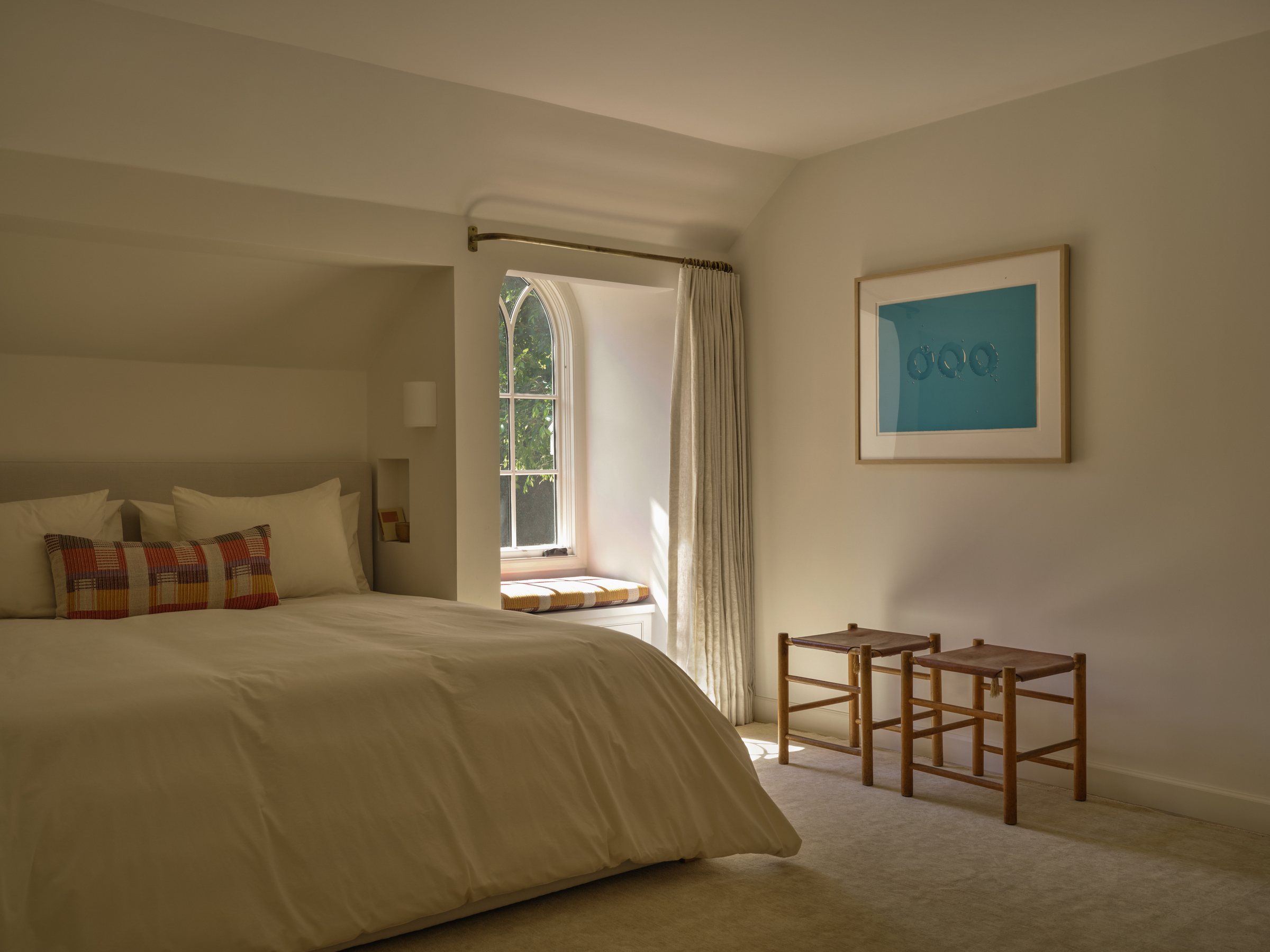 Bedroom with an arched window seat, linen curtains, and a framed photograph above the bed.