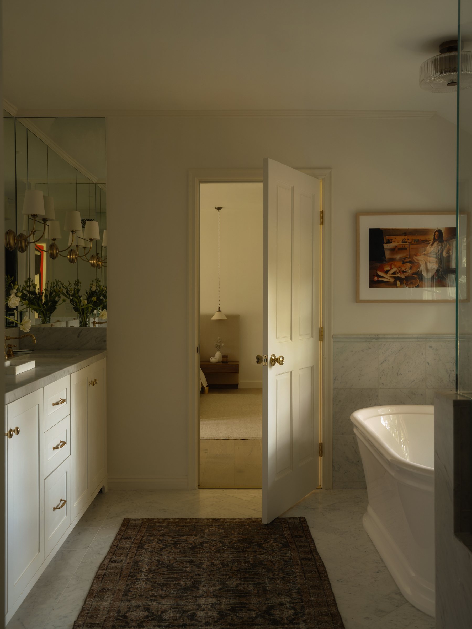 Freestanding tub beside a marble-tiled wall, doorway open to the bedroom.