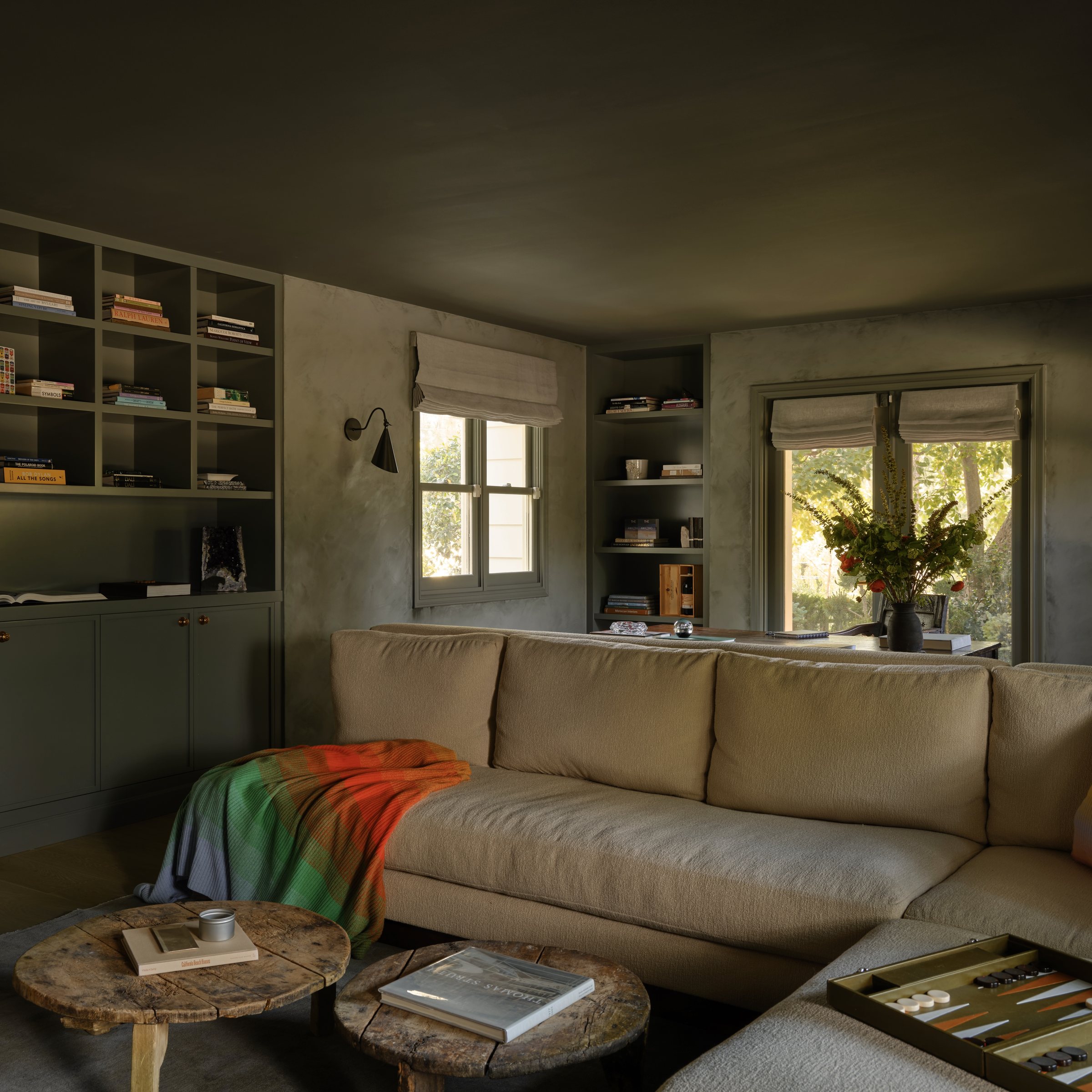 Olive-toned library with built-in bookshelves, a sectional sofa, and a game table.