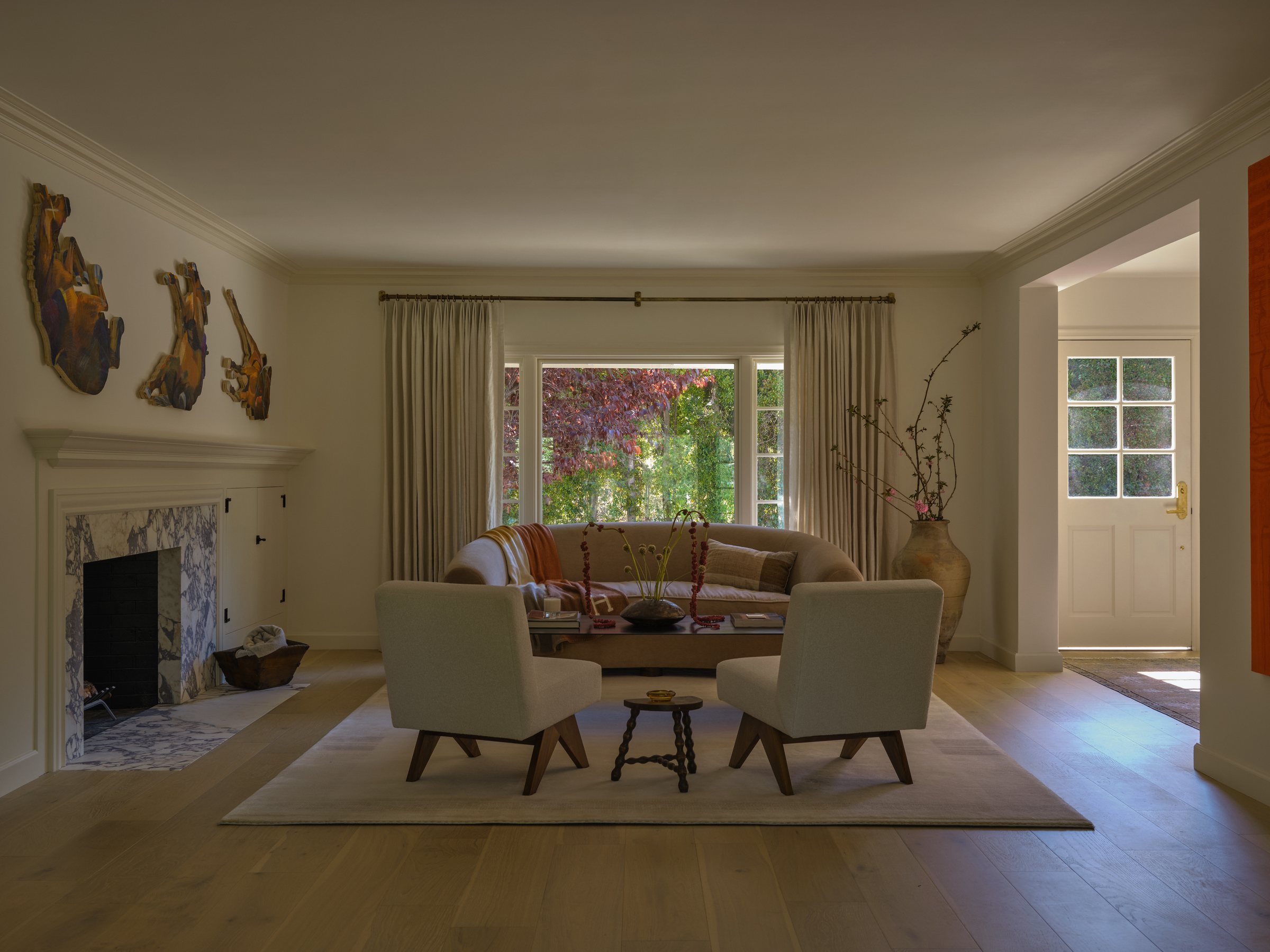 Living room with a stone fireplace, framed abstract wood sculptures, and two loveseats facing a marble coffee table.