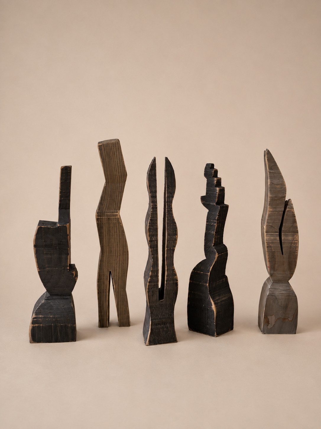 Five hand-carved wooden totems in varied abstract silhouettes and dark and natural finishes, standing side by side.