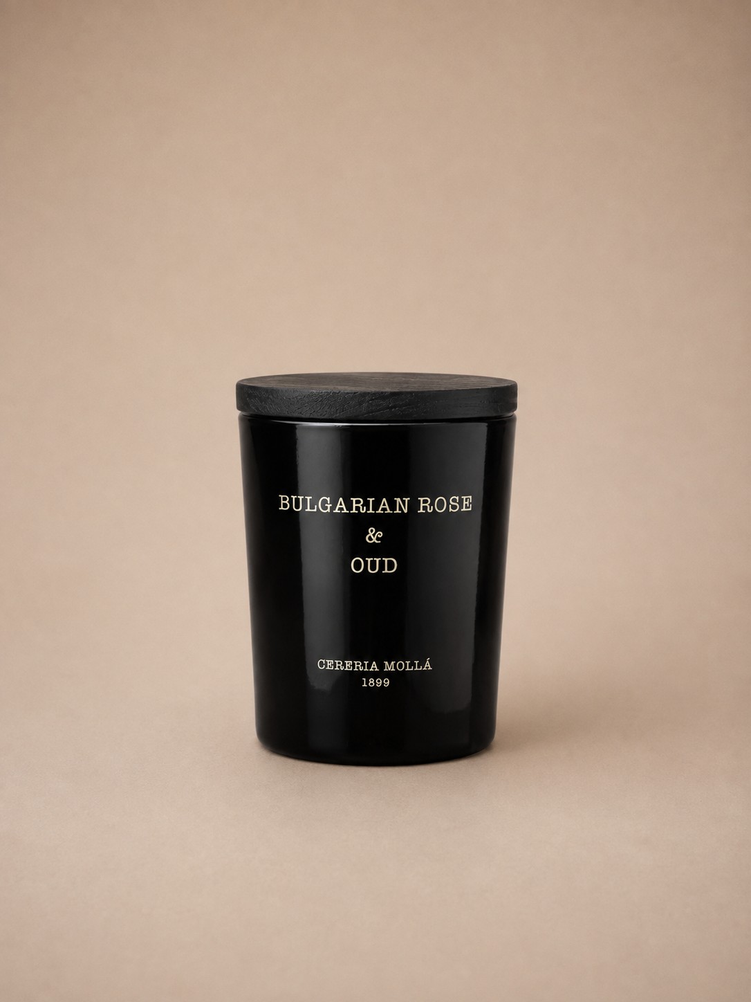 A black glass candle with a black wood lid, labeled Bulgarian Rose & Oud, by Cereria Mollá 1899.