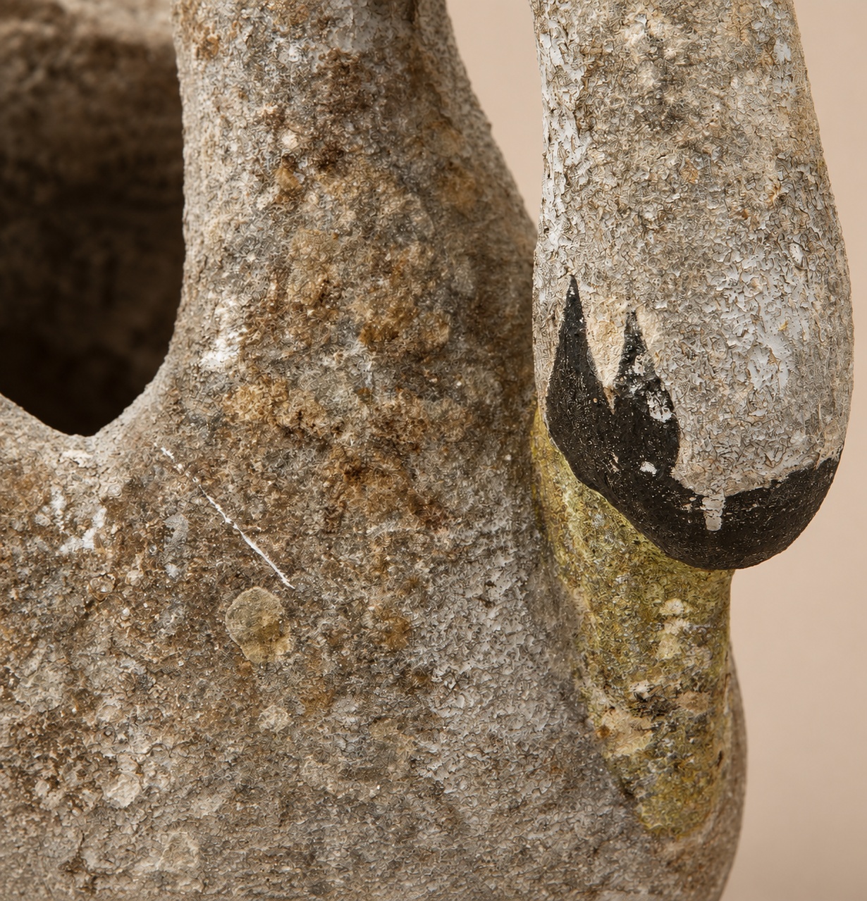 Close-up detail of a vintage concrete swan planter, showing the textured lichen patina and painted black-tipped beak.