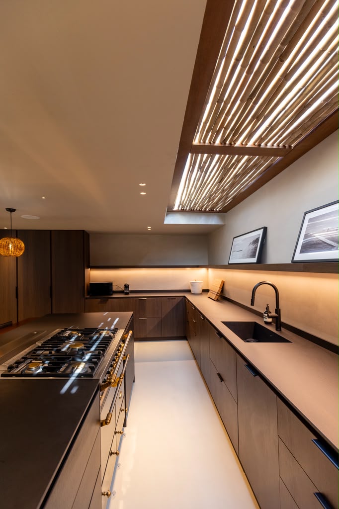 Kitchen with a black stone island, brass gas range, and a bamboo-slat skylight overhead.