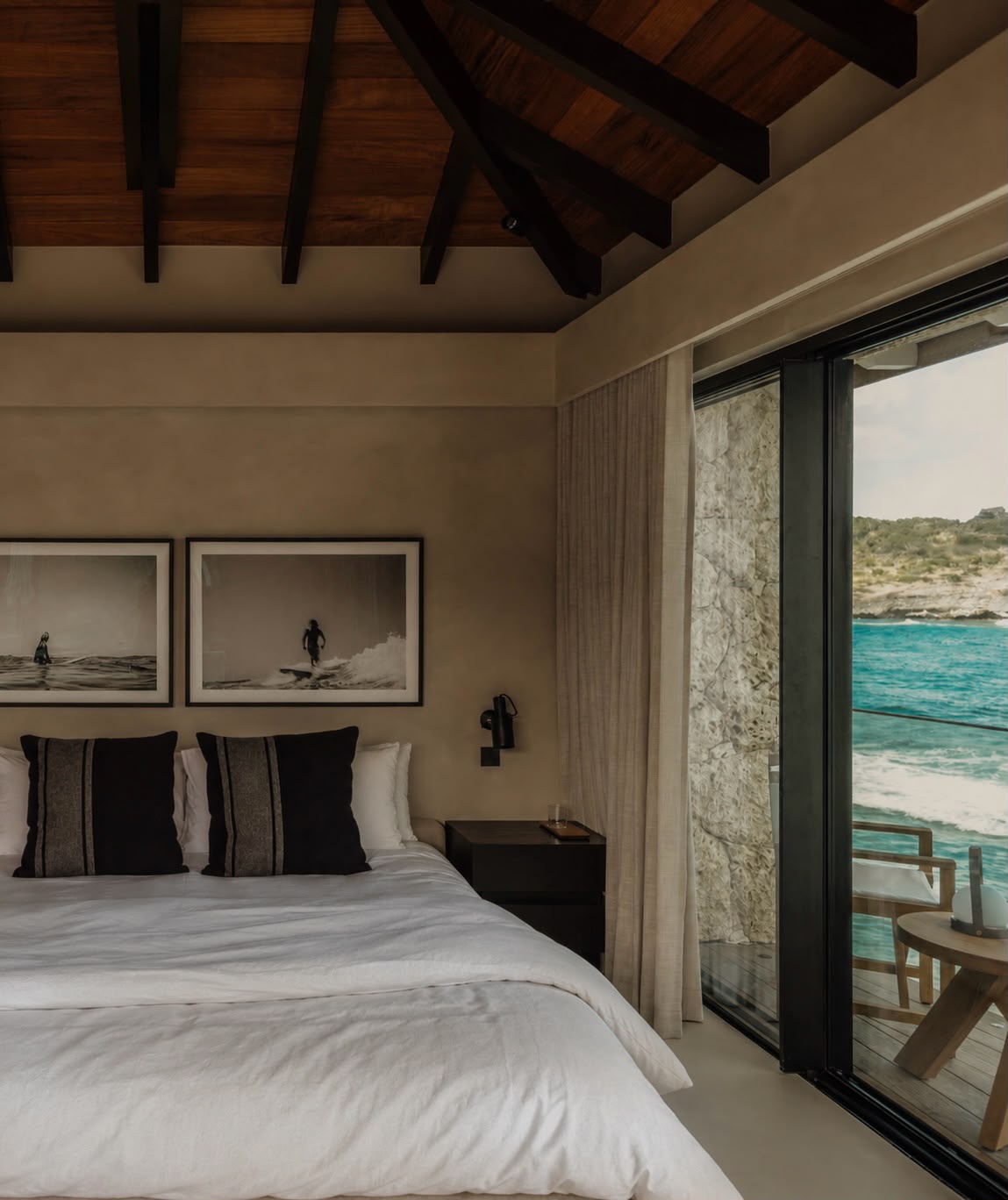 Bedroom with black-and-white surf photography above the bed and a sliding door open to the ocean deck.